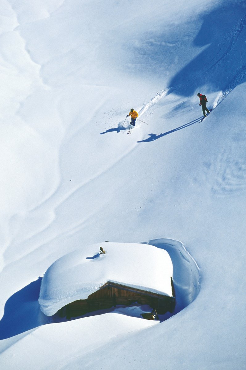 Snow Covered Alpine Hut And Skiers